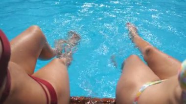 Otelin havuzunda kristal berrak su sıçratan dişi bacaklar. Havzanın kenarında oturan iki arkadaş güneşli bir günde tatilin tadını çıkarıyorlar. Yaz tatili ya da tatil kavramı. Yavaş çekim bakış açısı.
