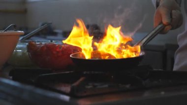 Profesyonel aşçının elindeki alevli tavada ayrıntılı görüş leziz flambe stili yemekler. Profesyonel aşçı sebzeleri tavada fırında pişiriyor. Yavaş çekim. Yakın çekim..