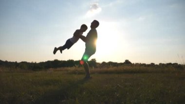 Babası oğlunun bir çayırda güneşli bir günde dönüyor. Baba döndürme bebeğe çevresinde doğa. Gün batımında sahada oynayan aile. Baba ve çocuk birlikte eğleniyor. Yavaş hareket kapatmak.
