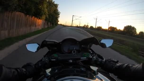 オートバイのライダーは日没時に村を通って田舎の道路に乗ります 郊外の国のルートでバイクを運転するオートバイの視点 バイカーが自転車を走るという視点 パブリック — ストック動画