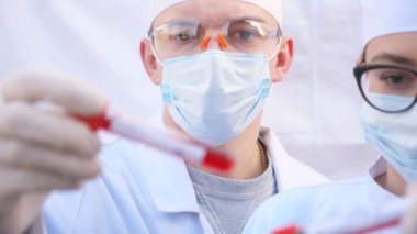 İki doktor koronavirüs için kan örnekleriyle test tüplerini inceliyor. Koruyucu eldivenli erkek ve kadın sağlık görevlileri kan örneklerini test ediyor. COVID-19 salgınından sağlık ve güvenlik hayatı kavramı.