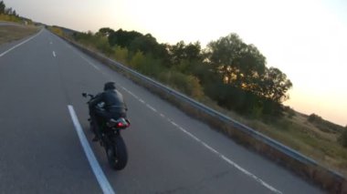 Günbatımında şehir yolunda motosikletle gezen motosikletliyi takip edin. Motosikletli otoyolda motosikletiyle yarışıyor. Yolculuk sırasında bisiklet süren adam. Yolculuk ve özgürlük kavramı. Hava görüntüsü.