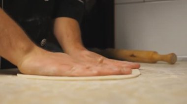 Lokantada ahşap bir yüzey üzerinde hamur işi oluşturan erkek kolları. Mutfak masasında pizza için un hamuru şekillendiren şefin elleri. Yemek hazırlama kavramı. Yavaşça kapat..