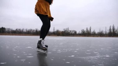 Kız bulutlu bir günde donmuş nehirde ya da gölde paten kayıyor. Doğada buz pateni pistinde kayan artistik paten giyen genç bir kadın. Soğuk kış havasında sporcu kadın eğitimi. Kış zamanı aktif bir eğlence. Yavaş çekim.