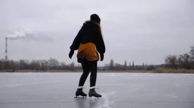 Buz yüzeyinde geriye doğru kayan buz patenli bir kadın. Genç kız kış günü donmuş nehirde paten kayıyor. Soğuk havada gölde sporcu kadın eğitimi. Kış mevsiminde aktif boş zaman.