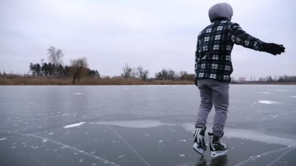 若い男は 屋外の氷の表面に滑るフィギュアスケートで光っている 曇りの日に凍った川でスケートする男 冬の寒さの中で湖でアクティブなレジャーをしているスポーツマン スローモーションを閉じる — ストック動画