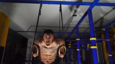 Spor salonunda jimnastik ringlerinde şınav çeken kaslı Afro-Amerikan sporcu. Güçlü bir Afrikalı atlet, kapalı alanda sıkı egzersiz yapıyor. Genç siyah jimnastikçi spor salonunda eğitim görüyor. Sağlıklı yaşam tarzı kavramı.