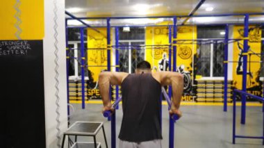 Modern spor salonundaki paralel barlarda şınav çeken kaslı sporcu. Spor kulübünde egzersiz yapan genç bir sporcu. Güçlü sporcu içeride sıkı çalışıyor. Aktif spor yaşam tarzı kavramı. Yavaşla.