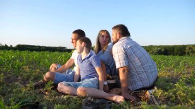 İki oğlu olan genç ebeveynler mısır tarlasında birlikte vakit geçiriyorlar. Çocuklu anne ve baba yeşil alanda oturuyor ve güzel doğanın tadını çıkarıyorlar. Aile mutluluğu kavramı. Yavaş çekim.