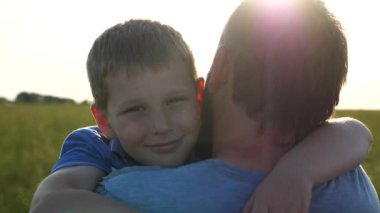 Kırsal kesimde küçük oğlunun elini tutan genç bir baba. Küçük gülümseyen çocuk kameraya bakıyor ve gün batımının arka planında babasına sarılıyor. Aile dinlenmesi kavramı. Kapat..