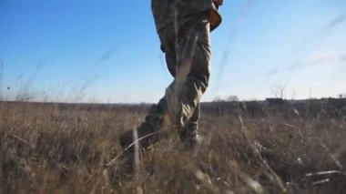 Güneşli bir günde, asker ayakkabısı giymiş genç bir askerin bacak çekimleri. Ukraynalı askerlerin erkek ayakları kırsal alandaki kuru otların arasından kahverengi çizmelerle geçiyorlar. Ukrayna 'da savaş. Yavaş çekim.