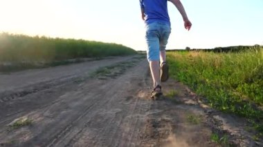 Kameralar, çayırda koşan ve mutlu bir yaz tatili geçiren mutlu çocuk için. Yerde koşan sandaletli küçük bir çocuğun erkek ayakları toz izi bırakıyor. Çocukluk konsepti. Yavaş çekim. Yakın çekim..