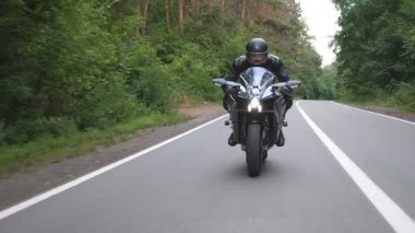 Kırsal Orman Yolu 'nda modern spor motosiklet süren kasklı genç bir adam. Motosikletli, tahta yolda motosikletiyle yarışıyor. Yolculuk sırasında bisiklet süren adam. Özgürlük ve macera kavramı. Ön görünüm.