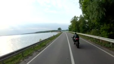 Motosikletli modern spor motosikletli göl kenarındaki yolda. Motosikletli yarış motosikleti yaz günü baraj yolunda. Nehir köprüsünden bisikletle geçen bir adam. Özgürlük ve yaşam tarzı kavramı.