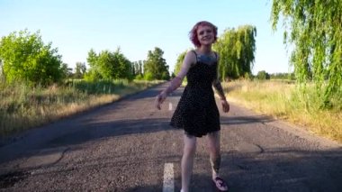 Siyah elbiseli genç hippi kadın kırsalda boş bir yolda yürüyor. Pembe saçlı mutlu punk kızı, kır yolunda gezerken aylak aylak dolaşıyor. Kaygısız kadın hippi dışarıda eğleniyor..