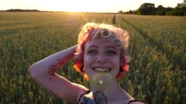 Pembe saçlı neşeli punk kızı görüntüsü kameraya bakıyor ve Buğday Çayırı 'nda blog için video kaydediyor. Kulak tünelleri olan neşeli hippi kız akıllı telefondan konuşuyor ve el sallıyor..