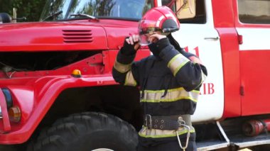 Üniformalı erkek itfaiyeci kaskını çıkartıyor ve itfaiye arabasının yanında duruyor. Genç bir itfaiyeci, büyük kırmızı bir kamyonun arka planında çıkan yangından sonra ekipmanları çıkartıyor. Hayat kurtarma kavramı