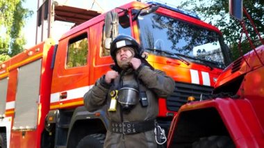 Üniformalı erkek itfaiyeci kaskını çıkartıyor ve itfaiye arabasının yanında duruyor. Genç bir itfaiyeci, büyük kırmızı bir kamyonun arka planında çıkan yangından sonra ekipmanları çıkartıyor. Hayat kurtarma kavramı