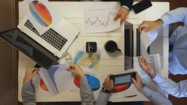 Male and female hands of entrepreneurs analyzing financial graphs at office. Group of young coworkers create corporate project sitting at table. Colleagues working on business development. Top view.