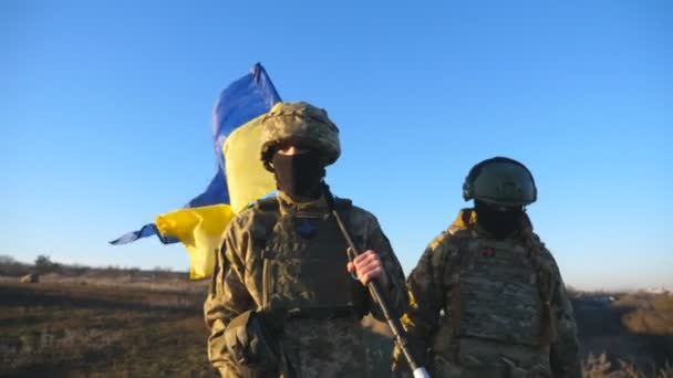 乌克兰陆军的男兵和女兵带着乌克兰国旗在战场上行走 落日时分 身穿军服的年轻男女带着蓝色和黄色的旗帜在草地上走着 对俄罗斯入侵的抵抗 — 图库视频影像