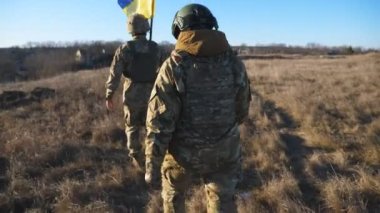 Ukrayna bayrağıyla yürüyen Ukrayna ordusunun kadın ve erkek askeri. Askeri üniformalı kadın ve erkek, Rus saldırısına karşı zafer işareti olarak Meadow 'da ulusal bayrak sallıyor..