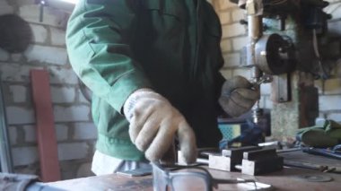 Genç tamirci atölyedeki metal detaylarıyla çalışmak için koruyucu gözlük takıyor. Üniformalı bir erkek tamirci garajında işini yapıyor. Bakım hizmeti kavramı. Dolly çekim ağır çekim
