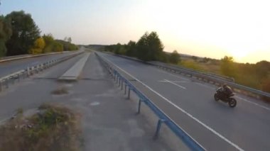 Günbatımında şehir yolunda motosikletle gezen motosikletliyi takip edin. Motosikletli otoyolda motosikletiyle yarışıyor. Yolculuk sırasında bisiklet süren adam. Yolculuk ve özgürlük kavramı. Hava görüntüsü.