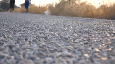 Kırsal yolda koşan iki kadının ayakları. Dışarıda koşan iki genç kız. Doğada birlikte antrenman yapan bayan sporcular. Sağlıklı aktif yaşam tarzı. Düşük açı Yavaş çekim.
