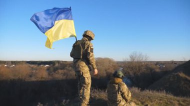 Ukrayna bayrağı kırsalda çimlerde oturan Ukrayna ordusundan bir çift. Kamuflaj üniformalı genç askerler ve dışarıda dinlenen ulusal afişler. Rus istilasına direniş. Dollyshot