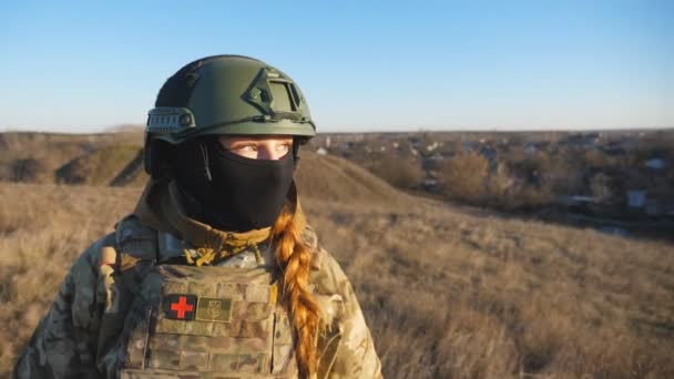 ヘルメットと日没を見てバラクラバでウクライナ軍の女性のドリーショット 若い女性の軍事医療現場に立っている ロシアの侵略に対する勝利 ヨーロッパでの戦争終結の概念 — ストック動画