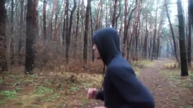 Sportif erkek koşucu sonbahar ormanında patika boyunca koşuyor. Orman yolunda koşan genç bir sporcu. Yağmurlu günlerde antrenman yapan güçlü bir sporcu. Sağlıklı aktif yaşam tarzı kavramı. Yavaş çekim.