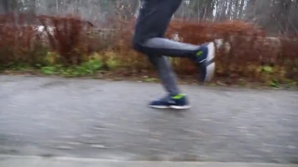 雨の日にトレイルに沿って走る若いスポーツマン アスファルト道路に沿ってジョギングするスポーティなランナーの男性フィート 屋外で強力で耐久性のあるアスリートトレーニング アクティブライフスタイルの概念 クローズアップ — ストック動画