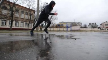 Yağmurda asfalt sahada mekik çalışması yapan genç sporcu. Bulutlu bir günde spor giyim sektöründe spor yapan bir adam. Açık havada egzersiz yapan güçlü bir erkek sporcu. Sağlıklı aktif yaşam tarzı kavramı.