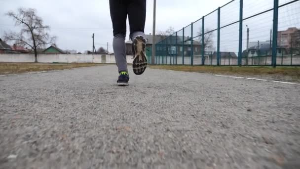 スポーティなランナーの男性フィートは 学校のスタジアムのパスでジョギングします スポーツフィールドで走る若いスポーツ選手の足 屋外で強力で耐久性のあるアスリートトレーニング アクティブライフスタイルコンセプト — ストック動画