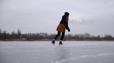 Genç kız bulutlu bir günde donmuş nehirde paten kayıyor. Sporcu kadın doğada buz pistinde kayan artistik patenlerle nallandı. Soğuk kış havasında gölde bayan patenci eğitimi. Açık havada aktif boş zaman.