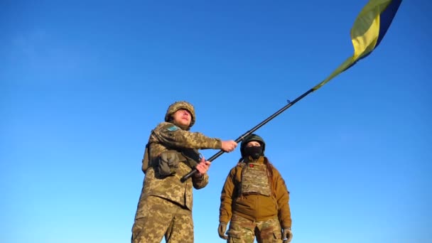 軍服の軍隊の人々は 青空に対してウクライナの旗を振っています 兵士たちはウクライナの国旗を掲げた ロシア侵略に対する勝利 侵入抵抗コンセプト スローモーション — ストック動画