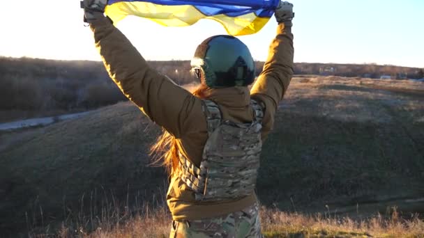 ユニフォームとヘルメットを着た女性兵士は 夕日に対する丘でウクライナの旗を掲げています 国営の黄色い青い旗を持っている軍医 侵略に対する勝利 侵入抵抗コンセプト — ストック動画