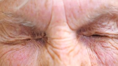 Yaşlı bir kadın kameraya bakıyor ve gözlerini fena halde bozuyor. Şaşırtıcı duygular gösteren geniş gözlü, buruşuk kadın yüzünü kapatın. Yüzünde hayret ifadesi olan bir büyükanne. Yavaş çekim.