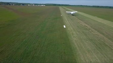 Eski uçak küçük havaalanındaki çim pistinden kalkıyor. Retro uçak kırsal pistte hareket ediyor ve uçuşa başlıyor. Spor uçakları havaalanından ayrıldı. Havacılık konsepti. Hava görüntüsü. İHA atışı.