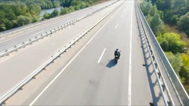 Bisikletçi yaz günü yol gezisi sırasında motosiklet sürüyor. Adam otoyolda modern spor motosikletle hızlı gidiyor. Motosikletli, kır yolunda bisikletiyle yarışıyor. Macera kavramı. Hava görüntüsü.