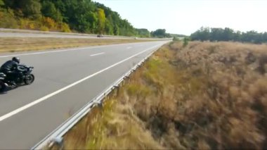Anayolda motosiklet süren motosikletliyi takip edin. Motosikletli, kır yolunda motosikletiyle yarışıyor. Yolculuk sırasında bisiklet süren adam. Yolculukta özgürlük ve macera kavramı. Hava görüntüsü.
