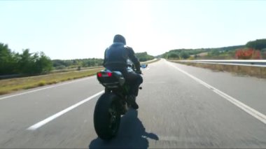 Bisikletçi yaz günü yol gezisi sırasında motosiklet sürüyor. Adam otoyolda modern spor motosikletle hızlı gidiyor. Motosikletli, kır yolunda motosikletiyle yarışıyor. Macera kavramı. Hava görüntüsü.