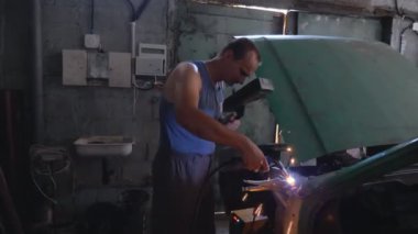 Koruyucu maske takan profesyonel bir tamirci. Garajda ya da atölyede çalışan tamirci. Adam servis aracına çarpmış. Sıcak kıvılcımlar uçuşuyor. Araba tamiri ve bakım konsepti.