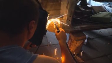 Koruyucu maske takan bir tamirci araba kaynakçılığı yapıyor. Garajda ya da atölyede çalışan tamirci. Adam servis araçlarını çalıştırıyor. Karanlıkta uçuşan parlak kıvılcımlar. Araba tamiri konsepti. Arka plan