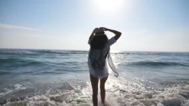 Sahilde koşan ve özgürlüğün tadını çıkaran mutlu genç bir kadın. Çekici, neşeli kız tropik bir tatil köyünde dinleniyor. Kaygısız kadın arka planda deniz manzarasıyla sahilde eğleniyor..