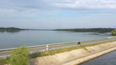 Yaz günü baraj yolunda motosiklet süren bir adam. Motosikletli, nehir köprüsünde motosikletiyle yarışıyor. Yolculuk sırasında bisiklet süren adam. Seyahat kavramı. Hava Görüntüsü Üst Görünüm.