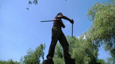 Yaşlı antrenör yüksek kütüklerin üzerinde duruyor ve Wing Chun kung fu 'sunu gösteriyor. Yetişkin erkek sporcu dövüş tekniklerini dışarıda tahta çubuklarla gösteriyor. Yaşlı adam yaz günü dövüş sanatları eğitimi alıyor..