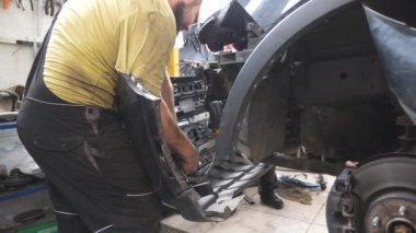 İki tamirci araba tamirinde ön tamponu söküyor. Profesyonel tamirciler tamirhanede ya da garajda tamir edilmeden önce otomobili söküyorlar. Araç bakımı ve tanı konsepti.