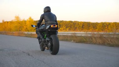Sonbahar otobanında modern motosiklet kullanan tanınmayan bir adam. Motosikletli, kır yolunda motosikletiyle yarışıyor. Seyahat sırasında motosiklet sürücüsü. Özgürlük ve macera kavramı. Arka görünüm.