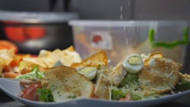 Aşçının erkek kolu Sezar salatasına rendelenmiş parmesan atıyor. Mutfakta beyaz tabakta. Mutfakta servis edilen lezzetli yemekler için eldiven hazırlayan bir el aşçı. Yemek pişirme kavramı. Dolly vurdu..